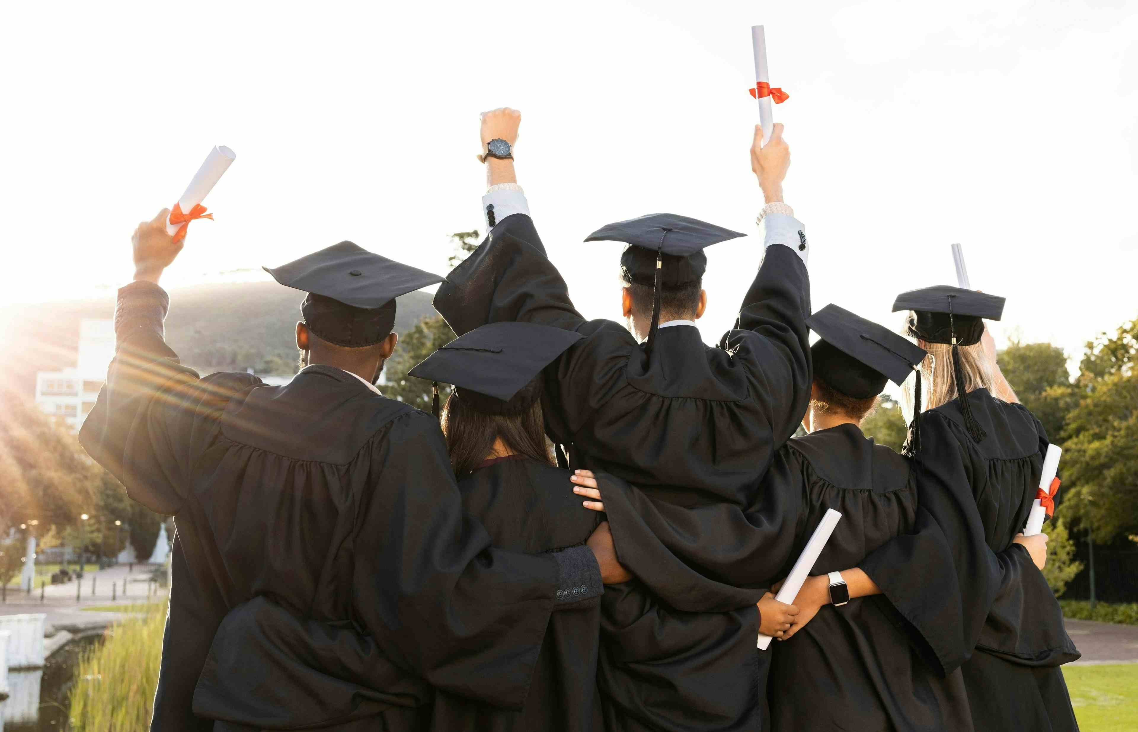 High School students in their graduation attire holding diplomas with their backs towards the camera