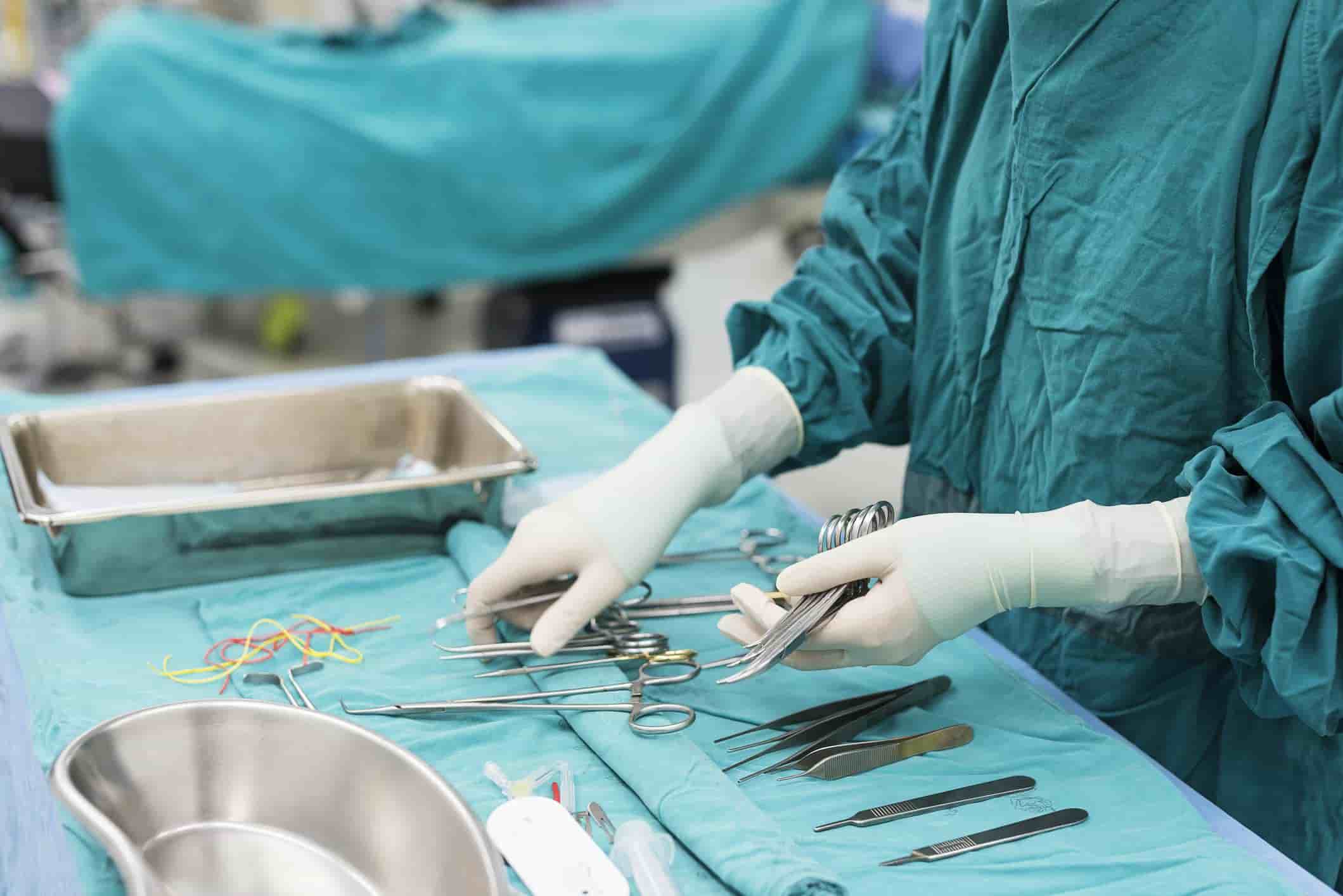 Close-up of a healthcare professional organizing surgical instruments in an operating room, wearing sterile gloves and scrubs.