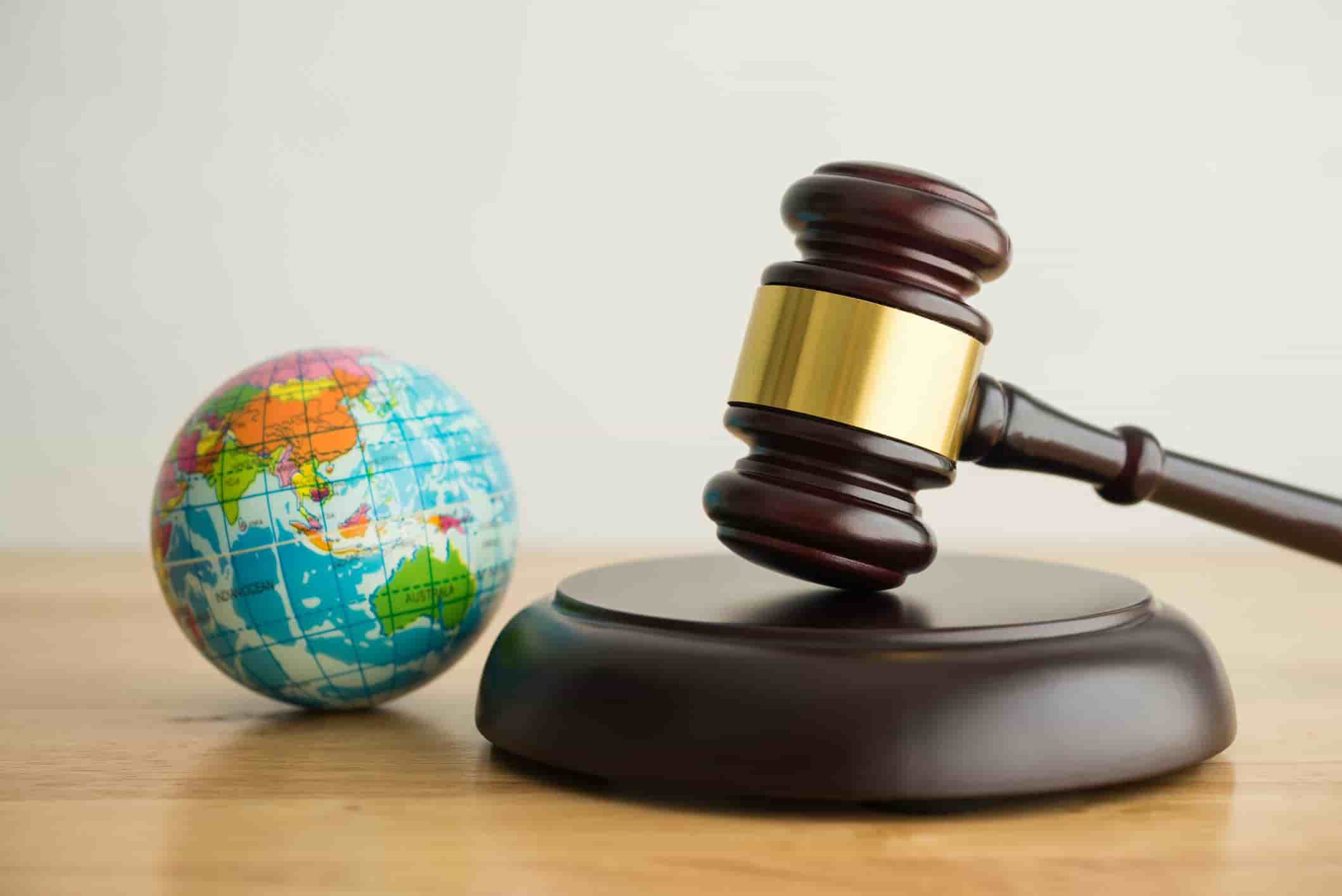 Wooden judge gavel next to a globe on a table, symbolizing international law or global justice.