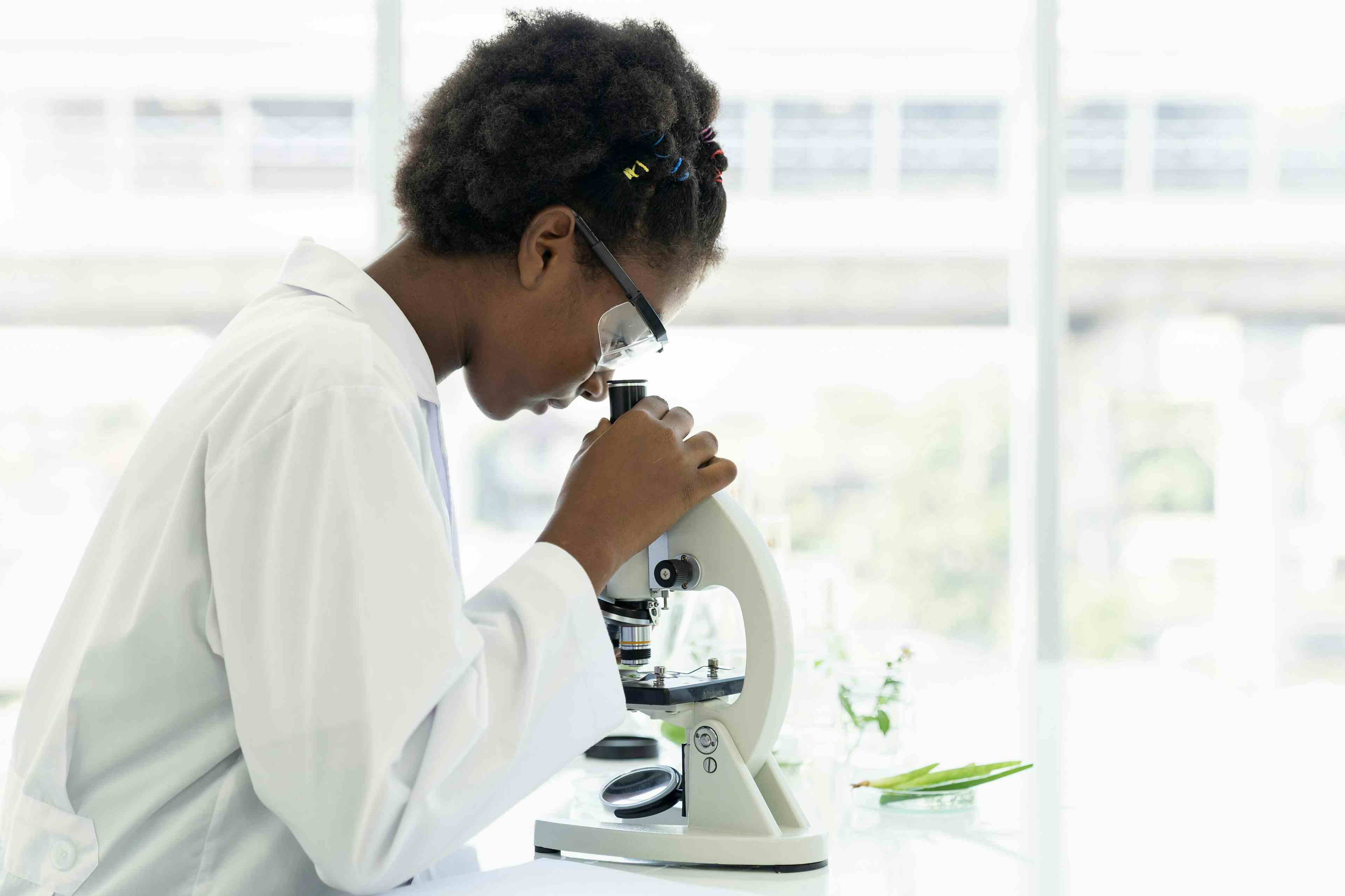 High School Student in white coat looking through microscope