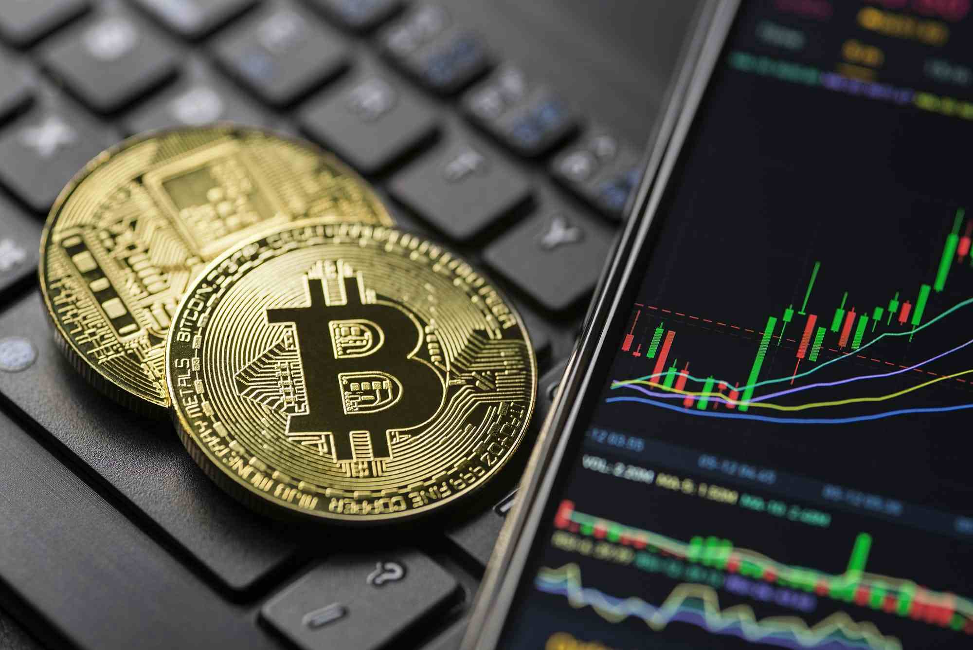 Bitcoin on computer keys and smartphone showing stocks